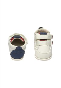 Zapatillas blancas con acentos en azul marino, que cuentan con dos correas de velcro, una parte frontal texturizada y un cuello acolchado. Material suave con una forma redondeada.