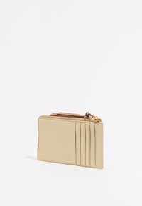 Portafoglio in pelle beige con superficie testurizzata, dotato di chiusura a zip e cinque scomparti per carte. Include un accento marrone nella parte superiore.