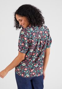 Blusa con pattern floreale e maniche corte a sbuffo, caratterizzata da uno sfondo blu scuro e fiori colorati nelle tonalità di rosso, verde e rosa.