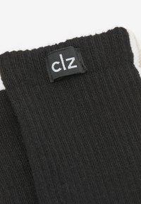 Svarta ribbade strumpor med en vit märkesetikett som visar "clz." Tyget verkar mjukt med en texturerad yta.