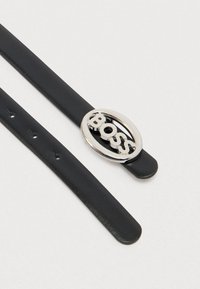 Μαύρη δερμάτινη ζώνη με ομαλή υφή και οβάλ ασημένια αγκράφα με τη λέξη «BOSS» σε έντονη, στιλιζαρισμένη γραμματοσειρά.