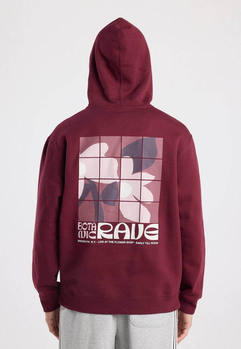 Sweat à capuche bordeaux avec une texture douce, présentant un graphique floral carré aux couleurs atténuées au dos et une typographie blanche audacieuse en dessous.