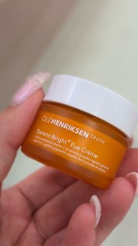 Mano sosteniendo un frasco naranja de Ole Henriksen Banana Bright Eye Crème con tapa blanca y etiqueta del producto visible.