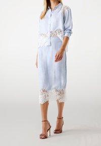 Jasnoniebieska bluzka z koronkowymi akcentami na ramionach, zestawiona z pasującą spódnicą z koronkowym wykończeniem. Uzupełniona brązowymi sandałami na obcasie.