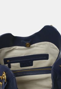 Interno di una borsa a tracolla in pelle blu navy, con fodera in tessuto crema, cerniera dorata e tasca a sbocco con dettagli del logo.