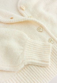 Zachte, roomkleurige gebreide sweater met mouwen en knopen met hartvormige gouden details op geribbelde manchetten en stof.