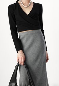 Svart långärmad topp i omslagstyp som matchas med en grå ribbad kjol. Outfiten kompletteras med en svart handväska och lager-på-lager-halsband.