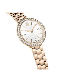 Montre en or rose avec un cadran rond, un fond blanc, des aiguilles dorées et des accents en cristal sur la lunette. Présente un bracelet de style maillon.