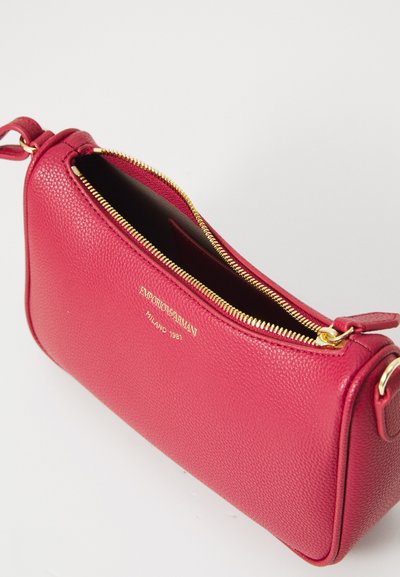 Red leather crossbody bag with a textured finish, gold zipper, and brand logo embossed on the front. Open top reveals black interior.