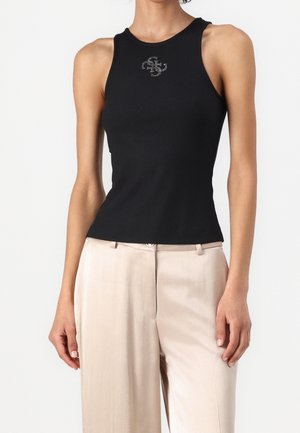 Czarny prążkowany top na ramiączkach z wysoką szyją i cienkimi paskami, ozdobiony srebrnym logo. W zestawie jasnobeżowe spodnie.