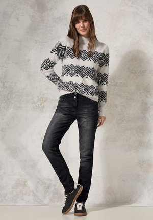 Grey and black patterned sweater with geometric designs, paired with dark denim jeans and black sneakers with brown soles.