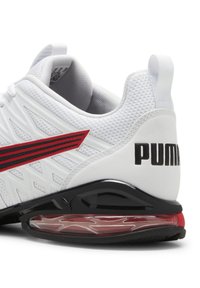 Weißer Sneaker mit einem strukturierten Mesh-Obermaterial, roten und schwarzen Designelementen, einer glänzenden schwarzen Sohle und einer sichtbaren Luftpolsterung in der Ferse.