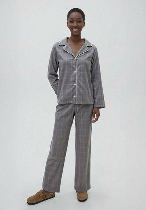 Conjunto de pijama de cuadros grises que incluye una parte superior abotonada con cuello y mangas largas, combinado con pantalones rectos a juego. Zapatos cómodos marrones.