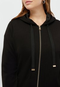 Felpa nera con zip, dal tessuto liscio, dotata di cappuccio, lacci neri con punte dorate e zip silver.