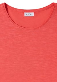 Chemise rose corail à manches courtes avec col rond et étiquette blanche indiquant "CECIL" cousue à l'intérieur du col.