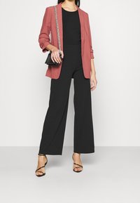 Pantaloni neri a gamba larga abbinati a una maglietta nera aderente e a un blazer color salmone. Accessoriati con una piccola borsa nera e tacchi con cinturini.