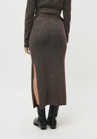 Jupe midi marron tricotée avec fente sur le côté, tissu texturé, taille élastique, associée à des bottes noires à hauteur de genou.