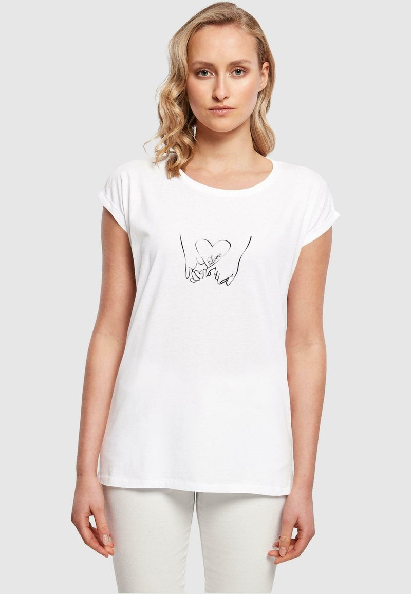 Hvid t-shirt med korte ærmer, der viser en sort linjetegning af to hænder, der danner en hjerteform med ordet "kærlighed" indeni.