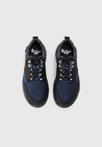 Pár sötétkék és fekete Dr. Martens cipő fényvisszaverő fűzőkkel, fém szemekkel és párnázott belső béléssel, felülről mutatva, fehér háttéren.