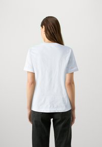 Camiseta de algodón blanca con mangas cortas, escote redondo y un ajuste relajado, combinada con pantalones de mezclilla oscuros. Tejido texturizado con un diseño minimalista.
