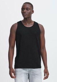 Svart bomullstopp med rund halsringning, utstyrt med en subtil logo på brystet. Tøyet virker glatt og lett.