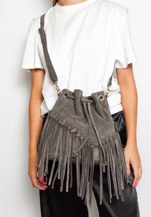 Borsa a secchiello in suede grigia con dettagli in frange, chiusura a coulisse e tracolla regolabile. Gli accessori in oro creano un contrasto.