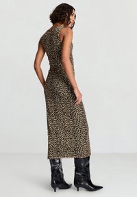 Maxikleid im Leopardenmuster, ärmellos, mit figurbetonter Silhouette, weichem Stoff und glatter Textur, kombiniert mit glänzenden schwarzen kniehohen Stiefeln.