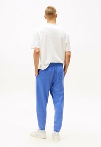 Weißes Baumwoll-T-Shirt mit kurzen Ärmeln, kombiniert mit blauen Sweatpants mit Taschen und elastischen Bündchen, getragen mit weißen Turnschuhen.