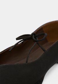 Musta nahkainen ballet-tossu pyöreällä kärjellä, jossa on pieni ohut pitsiköynnös ja sileä sisävuori. Minimalistinen muotoilu.
