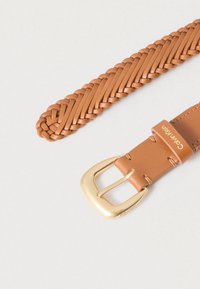 Ζώνη από πλεκτό δέρμα σε ταμπά απόχρωση με χρυσή αγκράφα, διαθέτοντας λείο φινίρισμα και λεπτομερές πλέξιμο κατά μήκος του ιμάντα. Ετικέτα εμπορικού σήματος ορατή στο δέρμα.