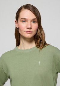 Ljusgrön stickad tröja med rund halsringning. Har en liten broderad logotyp på vänster bröst. Mjuk textur, avslappnad passform.