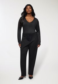 Czarny body z długim rękawem, z głębokim dekoltem w kształcie V, w połączeniu z czarnymi spodniami o wysokim stanie. Materiał wydaje się gładki i dobrze ustrukturyzowany. Czarne buty na szpilkach.