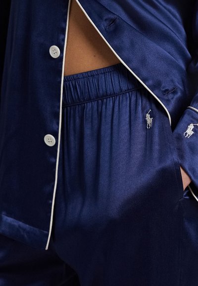 Navy satijnen pyjamaset met een overhemd met knopen en witte bies en broek met elastische tailleband, beide met geborduurde logo's.