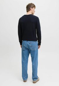 Chemise rayée marine à manches longues associée à un jean bleu clair à coupe décontractée. La tenue présente un design casual et une apparence en coton texturé.