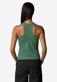Top verde a coste con scollatura rotonda e design racerback, silhouette aderente e texture liscia, abbinato a pantaloni cargo neri.