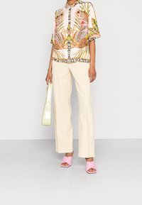 Blouse à manches courtes en tissu rose clair avec imprimé léopard et motif végétation tropicale, associée à un pantalon large crème et des sandales roses.