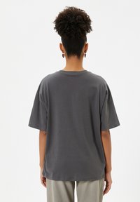 T-shirt in cotone grigio con maniche corte e vestibilità rilassata. Collo tondo e texture morbida. Indossato con pantaloni chiari.