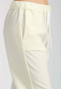 Pantaloni color crema con cintura elastica e dettagli nelle tasche frontali, mostrati su una persona dalla vita fino a metà coscia.