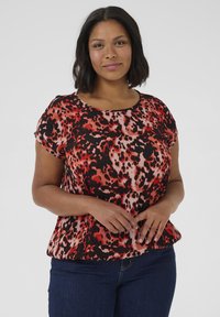 T-shirt à manches courtes avec un imprimé animal rouge et noir sur un tissu léger. Encolure bateau, coupe décontractée et ourlet légèrement évasé.
