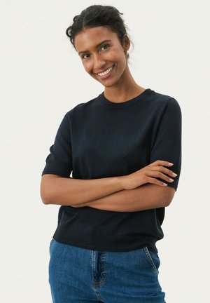 Navy blue knitted short-sleeve sweater with a round neckline, featuring a relaxed fit and subtle texture, worn with blue denim jeans.
