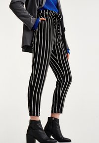 Pantalon rayé noir et blanc avec une taille haute, une coupe fuselée et des chevilles retroussées, accompagné de bottines noires.