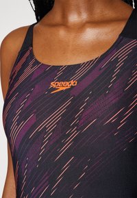 Maillot de bain Speedo avec une base noire ornée de motifs abstraits vibrants en violet et orange. Le matériau est lisse et présente un design à dos nageur.