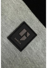Grijs en zwart gebreide stof met een rechthoekig zwart rubberen patch met verhoogd geometrisch ontwerp en het ingedrukte woord "GARCA".