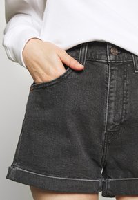 Shorts de mezclilla negra con una cintura alta, puños enrollados y bolsillos laterales. Presentan cierre de un solo botón y detalles cosidos en la tela.