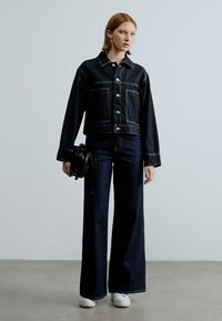 Fekete farmerdzseki kontrasztos varrással, rövidített kialakítással, nagy első zsebekkel. Magas derekú, bő szárú sötét farmernadrággal és fehér tornacipővel párosítva.