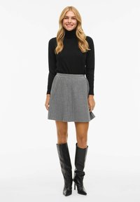 Černý rolák spojený se šedou plisovanou sukní, doplněný vysokými černými botami. Moderní střih a strukturovaná látka.