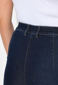 Jeans de mezclilla oscura de tiro alto con una amplia cinturilla elástica, costuras en contraste y una textura suave sin adornos visibles.