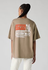Beige oversized T-shirt featuring red and white graphic print with text "LEVI'S® AUTHENTIC WESTERN WEAR ORIGINAL" and cactus design.