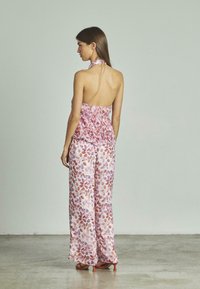 Combinaison florale dans des tons de rose et de violet, présentant un corsage smocké, un pantalon large et une encolure halter. Tissu léger.