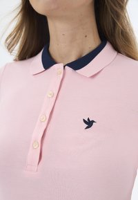 Svetle růžová polo košile s námořnickým modrým límcem, pěti knoflíky a malým námořnickým ptáčkem na levém prsu. Texturovaná tkanina.